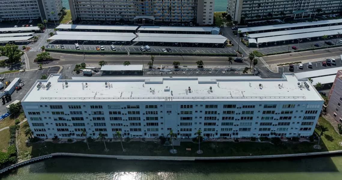 Aerial view of a large waterfront Southwest Florida condo building with a new white reflective roof installed by Seacoast Building & Design